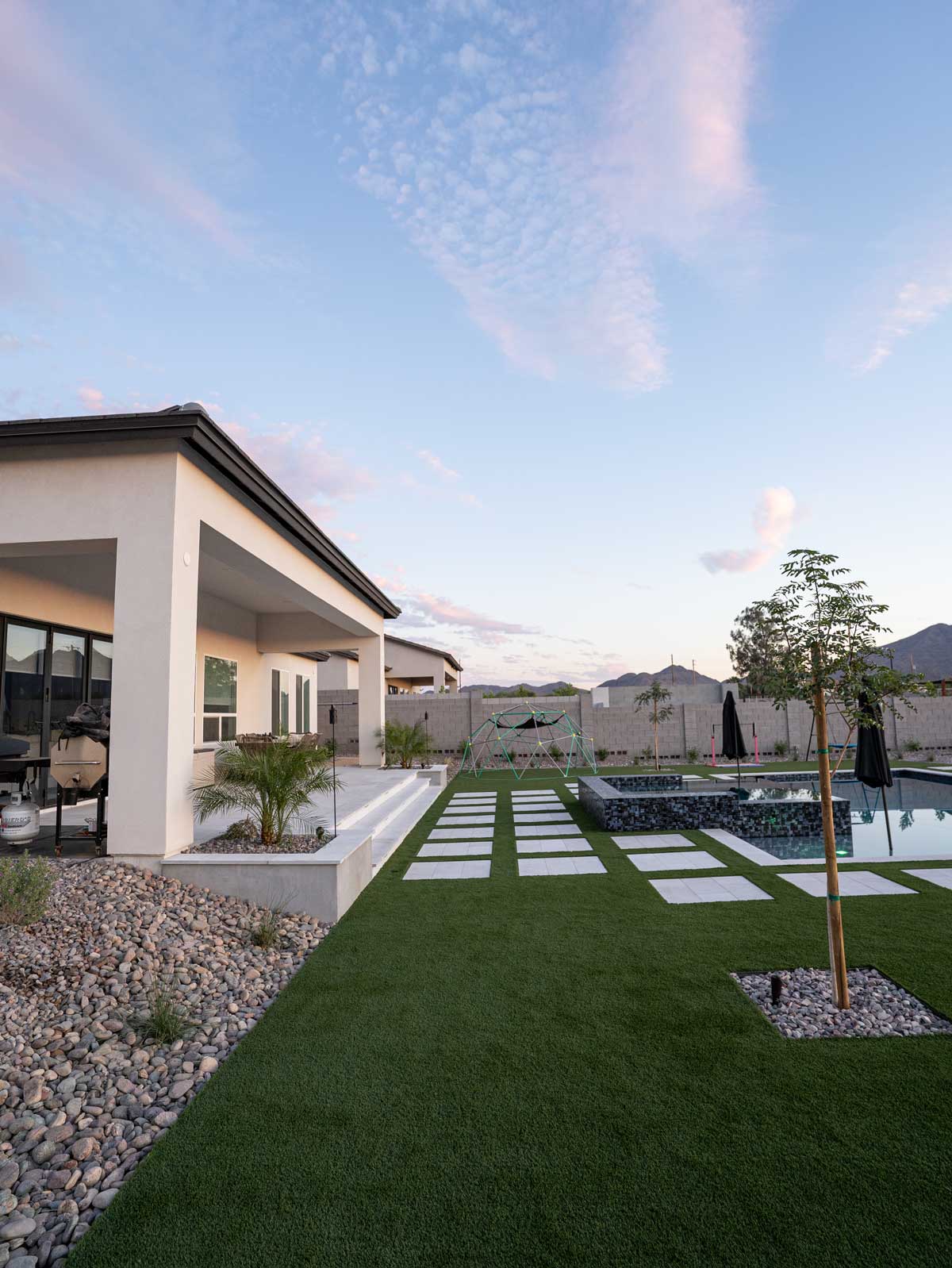 Modern Queen Creek backyard with artificial turf, floating pavers and pool with glass-tile spa