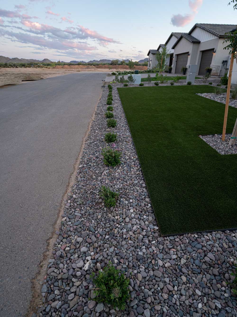 Front yard artificial turf bordered by river rock and desert shrubs along street, Queen Creek AZ