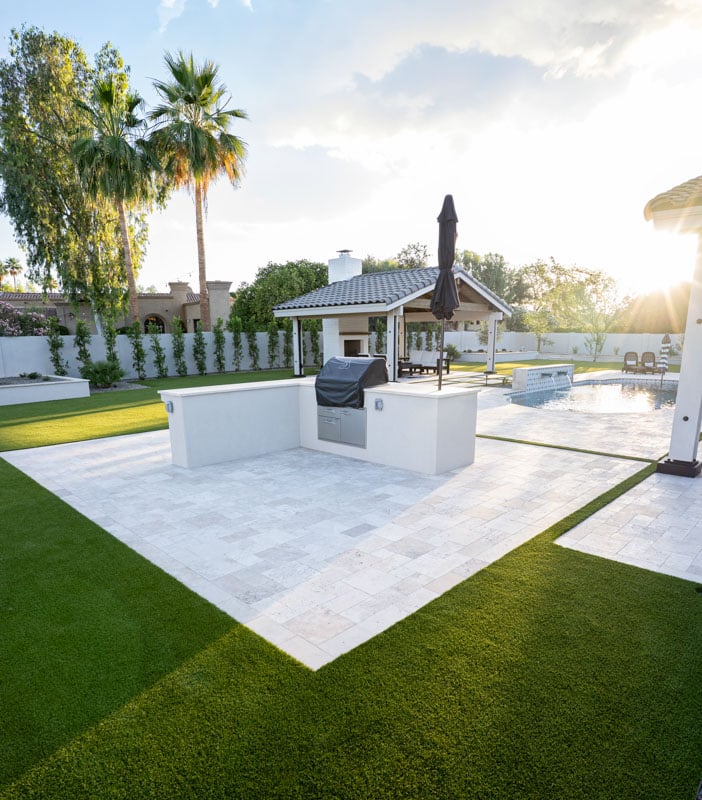 Built-in outdoor BBQ island on travertine pavers surrounded by artificial turf in a Scottsdale backyard
