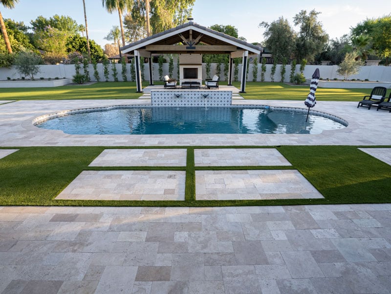 Freeform pool with star-tile water feature wall, travertine paver deck, and artificial turf panels in a Scottsdale backyard