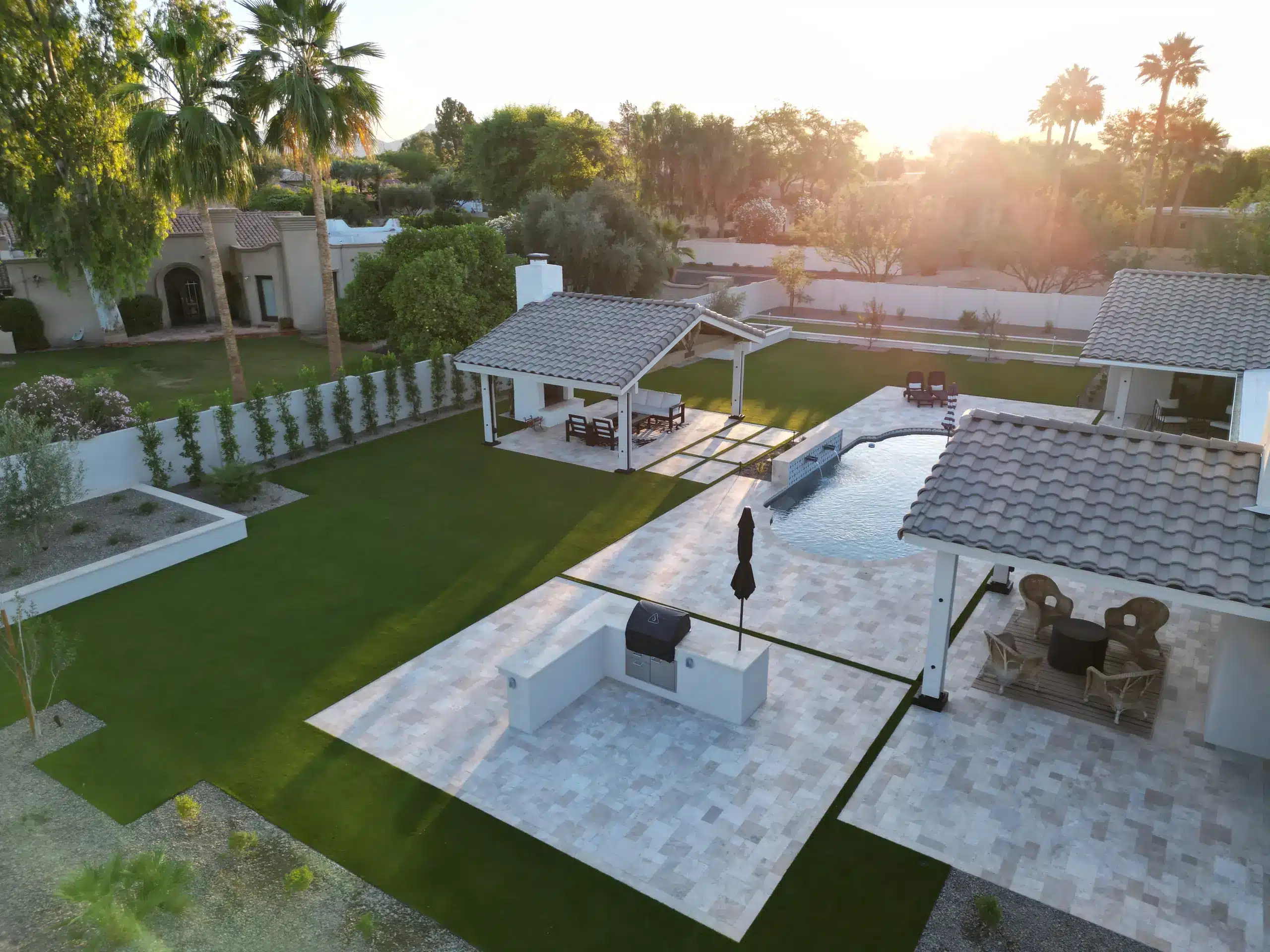 Aerial view at sunset of a Scottsdale backyard with artificial turf, a large-format paver patio, an outdoor kitchen and two ramadas